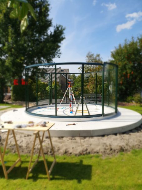 Ein runder, umzäunter Spielplatz mit einer Schaukel und einem Tisch im Freien.